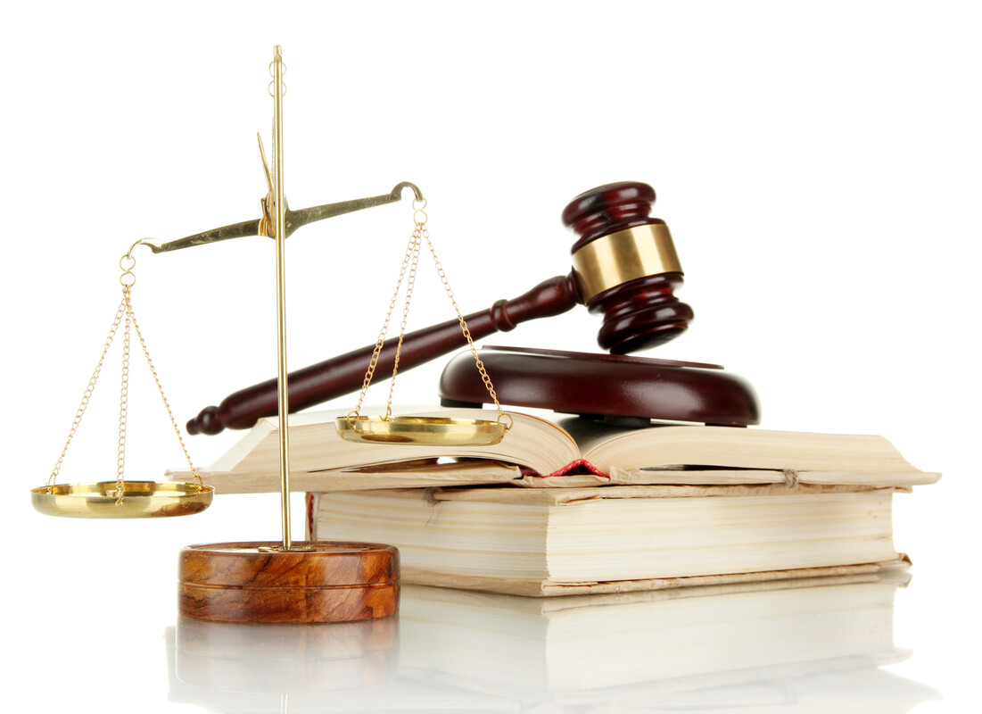 Bilancia in ottone con piatti dorati su base di legno e martelletto da giudice appoggiato su libri aperti, sfondo bianco